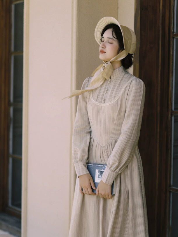Beige vintage long sleeve dress with high neck, lace detail and flowing maxi skirt styled with a bonnet