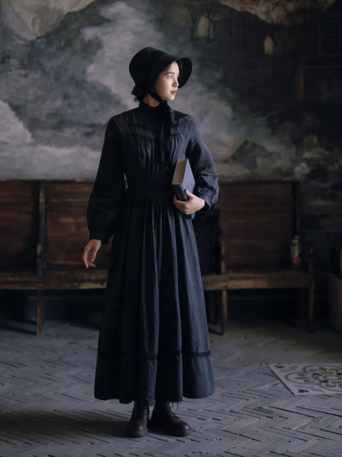 Full-length black gothic dress with high neckline, long sleeves and flowing skirt in an antique setting