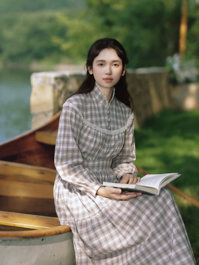 Gray plaid vintage maxi dress with high neckline, lace trim and long sleeves styled beside a lakeside boat