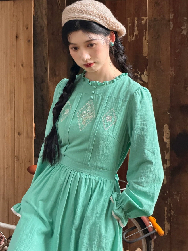 Close-up of mint green embroidered cottagecore dress with ruffle neckline, covered buttons and long sleeves