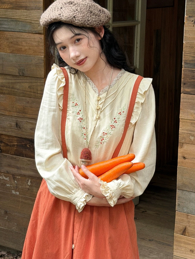 Women’s embroidered cream blouse with ruffled sleeves and terracotta suspender skirt in a rustic setting