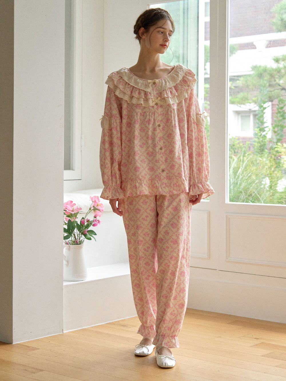 A relaxed full-body shot of a model in a cottagecore-style pink floral nightgown set with flowy pants and delicate lace accents.