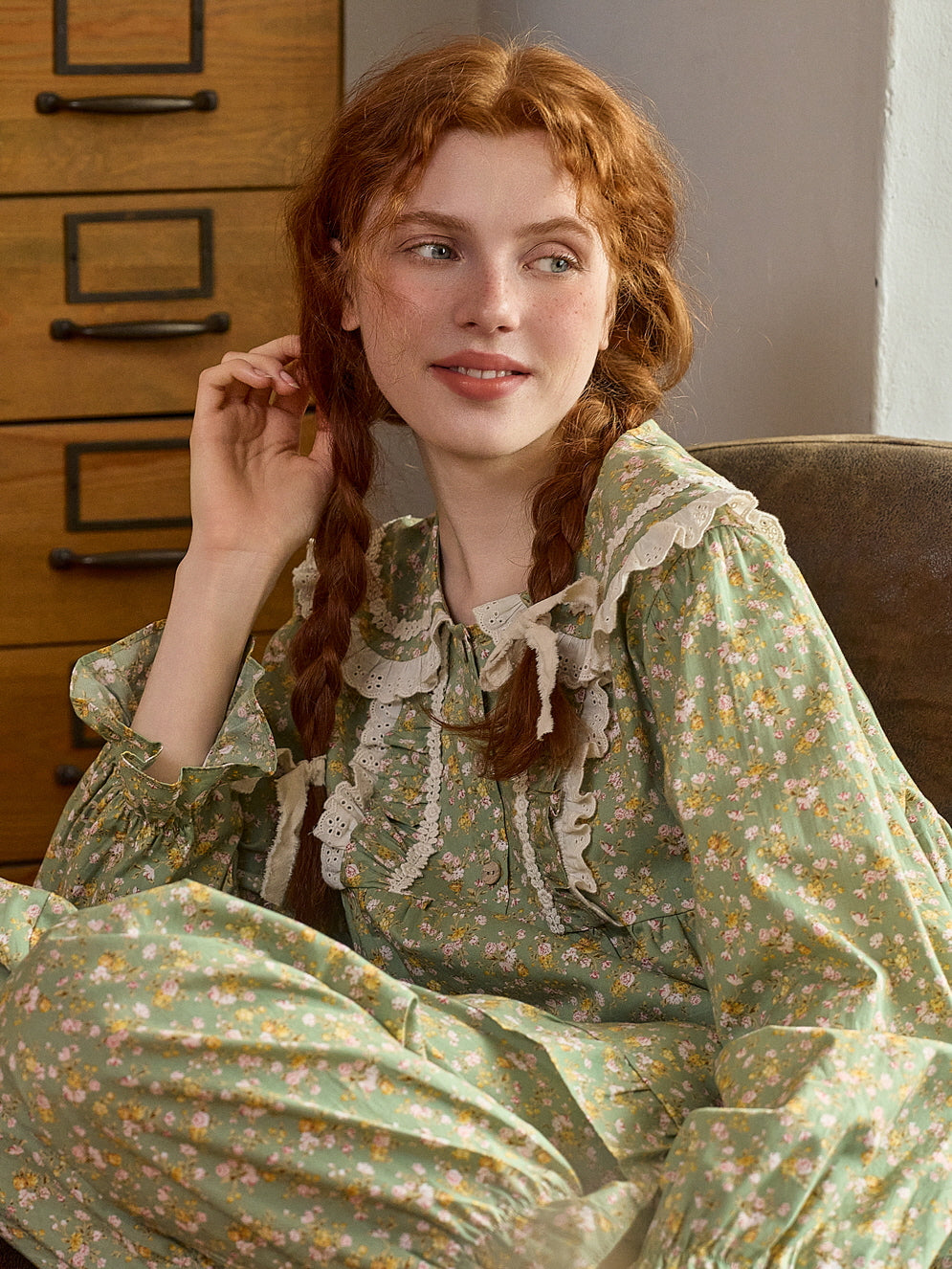 A cozy, seated pose in a green floral loungewear set with lace and ruffle details, capturing a relaxed, vintage-inspired fairytale vibe.