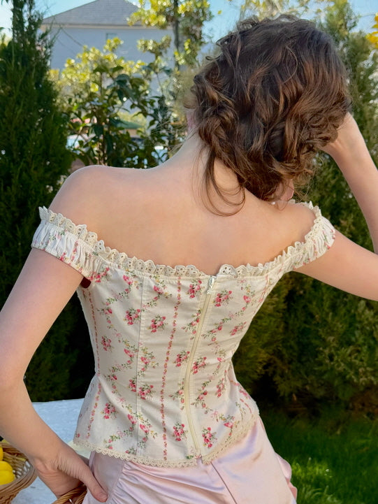 Back view of floral off-shoulder corset top with lace trim, styled with a pastel pink ruched satin skirt – romantic vintage fairytale outfit in a spring garden setting