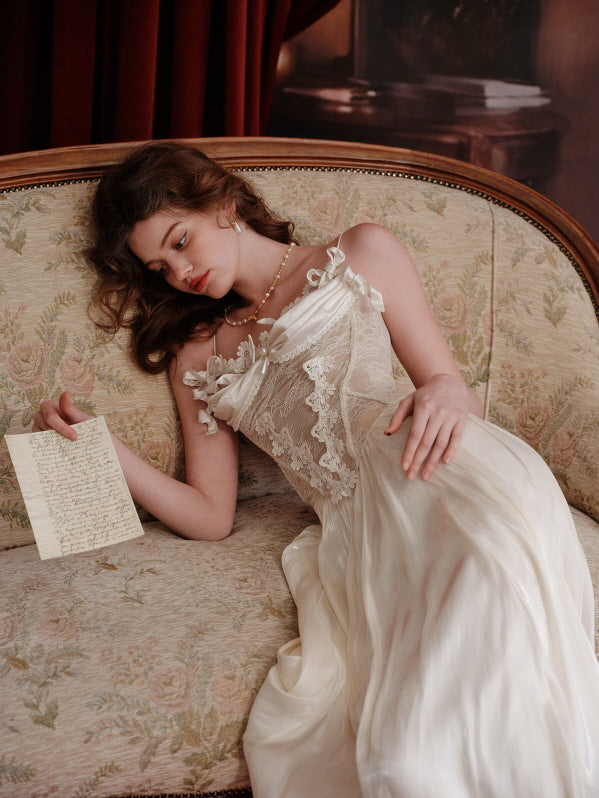 Romantic lace corset with floral embroidery and satin ribbon detail, worn by a model lying on a vintage rose-patterned sofa holding a handwritten letter, evoking a dreamy fairytale mood.