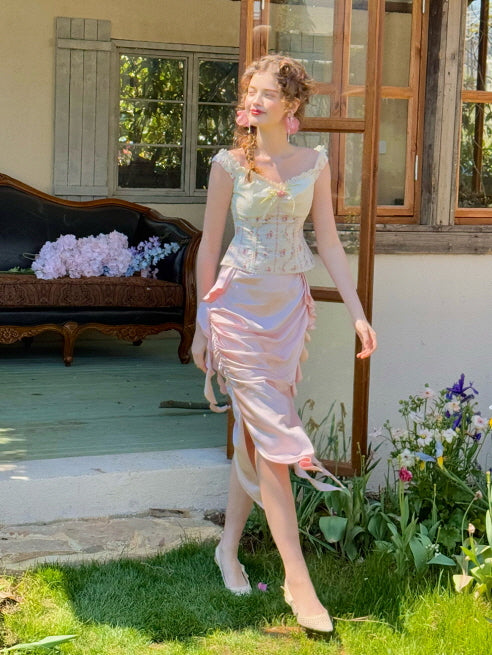 Romantic pastel pink ruched satin skirt with side ribbon details, styled with a floral corset top while walking through a flower garden – fairytale spring outfit for women