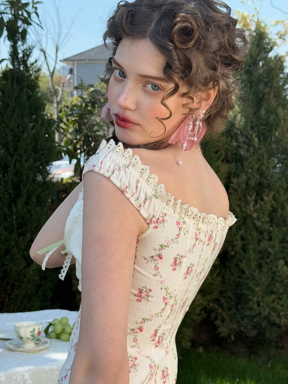 Close-up of vintage floral off-shoulder corset top with lace trim and pink bow earrings – romantic fairytale-inspired women’s styling in a garden setting