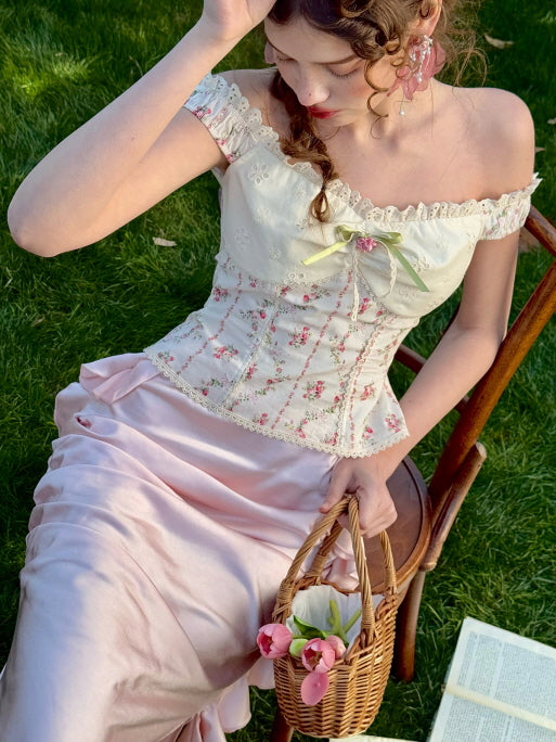 Romantic pink satin skirt with soft drape, styled with a floral off-shoulder corset top and ribbon basket in a spring garden – vintage fairytale cottagecore outfit for women