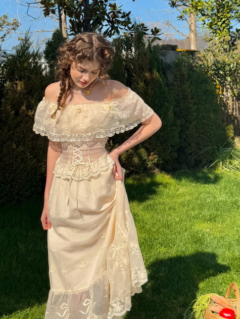Woman wearing an off-shoulder ivory lace corset dress holding the skirt delicately in a sunlit garden – romantic vintage outfit with floral embroidery and elegant silhouette