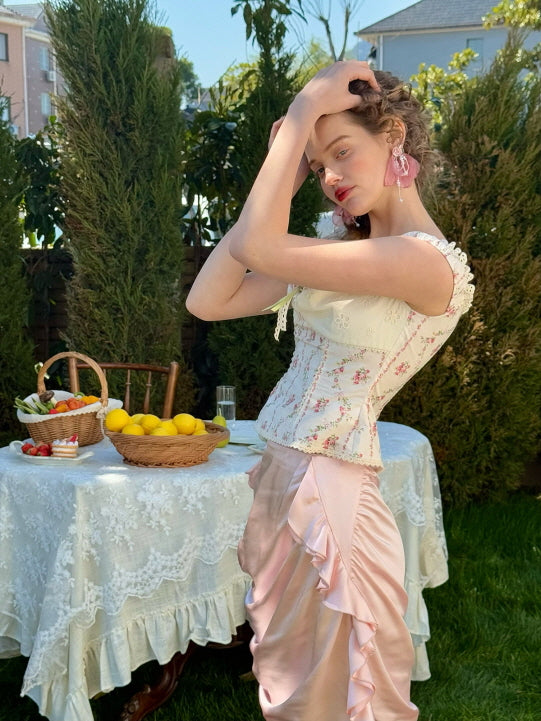 Side view of pastel pink satin skirt with ribbon ruched detail, paired with a floral lace-trim corset top – romantic vintage-inspired women's spring outfit in garden setting
