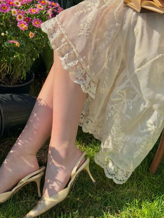 Close-up of vintage lace dress hem with floral embroidery and ruffle trim, styled with elegant heels in a garden setting – romantic fairytale aesthetic for women