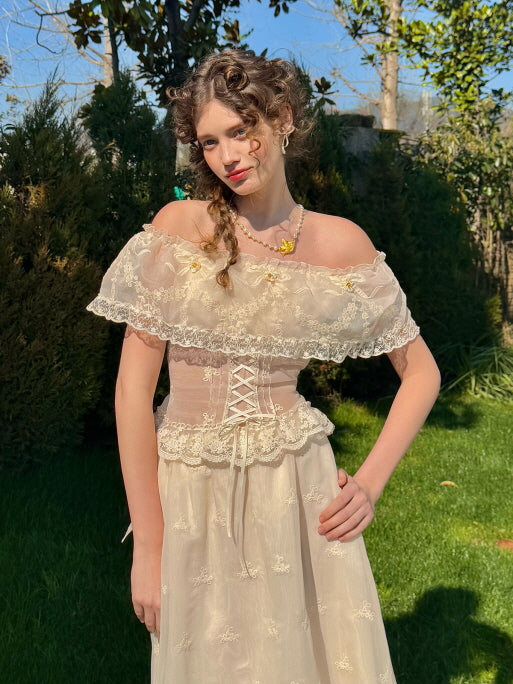 Romantic off-shoulder lace corset dress with floral embroidery and ribbon detail, styled with vintage curls and jewelry in a sunlit garden – fairytale-inspired women's outfit