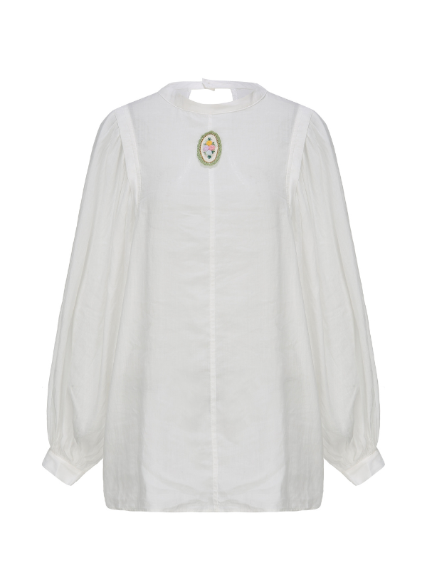 Flat lay of a puff-sleeve white blouse with a round neckline and floral brooch, designed for a romantic vintage or cottagecore-inspired look.