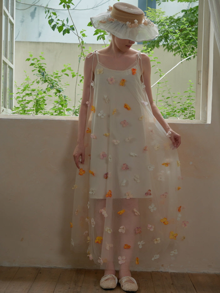 A woman in a fairytale-inspired sheer dress with colorful 3D floral appliqués stands by an open window, exuding a soft fairycore aesthetic.