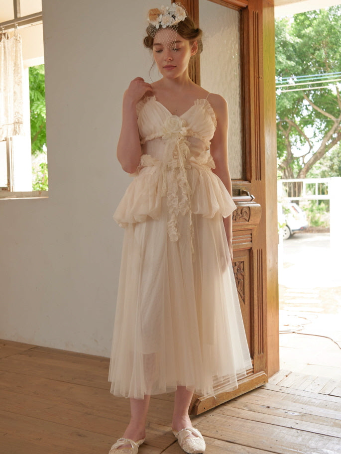 A young woman in a delicate ivory tulle dress with floral ruffle details stands gracefully indoors, embodying a dreamy fairycore aesthetic.