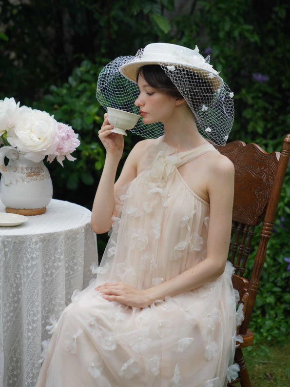 Model in a soft beige tulle dress with 3D floral details sips tea in a garden, evoking a serene vintage-inspired fairycore moment.