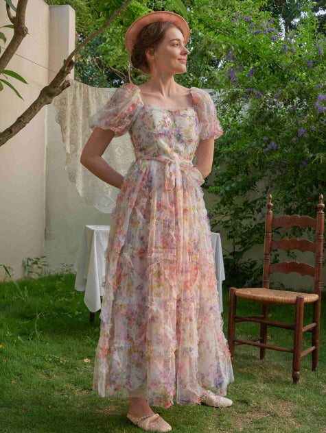 Wearing a vintage-inspired pink floral dress with layered tulle, the woman smiles softly in a cottage garden, exuding romantic elegance.