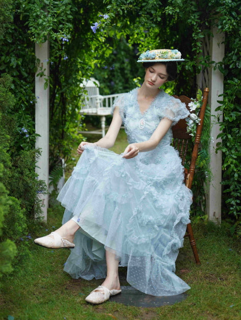 A young woman in a pale blue ruffled lace dress sits gracefully in a garden archway, embodying a soft princesscore and vintage aesthetic.