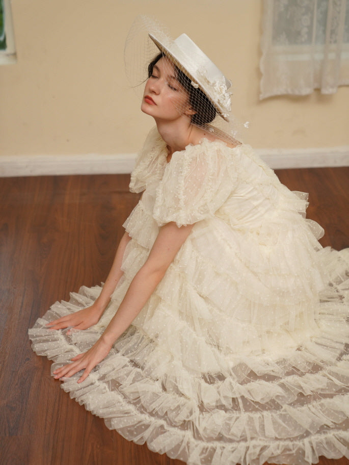 Model kneels gracefully in a layered ivory tulle dress with puff sleeves, capturing a dreamy princesscore look in a vintage-inspired setting.