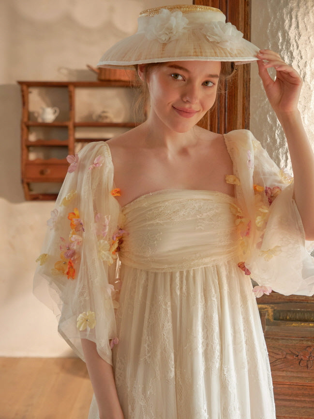 A model gently lifts a wide-brimmed hat while wearing a floral-appliqué sheer sleeve dress, radiating a soft princesscore aesthetic.