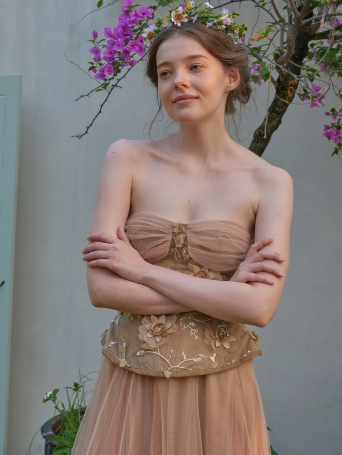 Close-up of a model in a romantic nude-toned tulle dress with floral embroidery, styled with a delicate flower crown in a cottage garden.