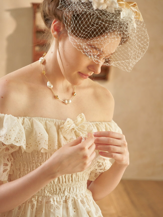 Close-up of a woman wearing a lace-trimmed off-shoulder dress with a pearl bow brooch, styled in a dreamy princesscore aesthetic.