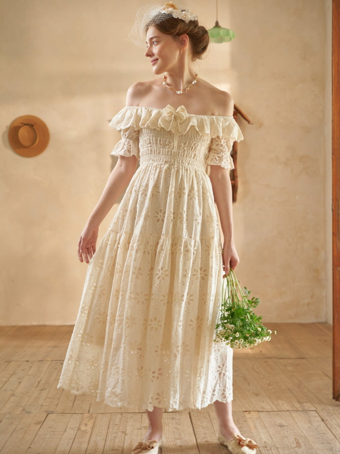 A woman in a vintage off-shoulder eyelet dress smiles gently while holding daisies, evoking a dreamy fairytale cottagecore vibe.