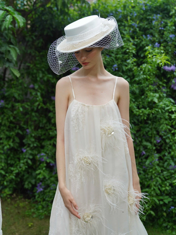 Close-up of a romantic cream dress with floral feathers and sequins, styled with a vintage hat for a dreamy fairy  garden look.