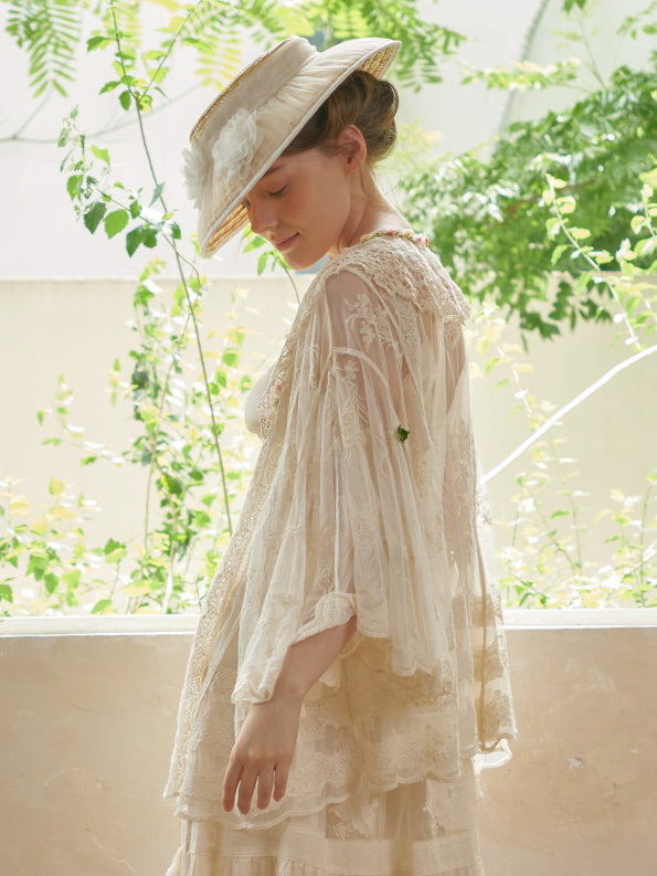 The model tilts her head with a serene smile, wearing a scalloped lace robe that flows gently in a vintage fairycore garden setting.