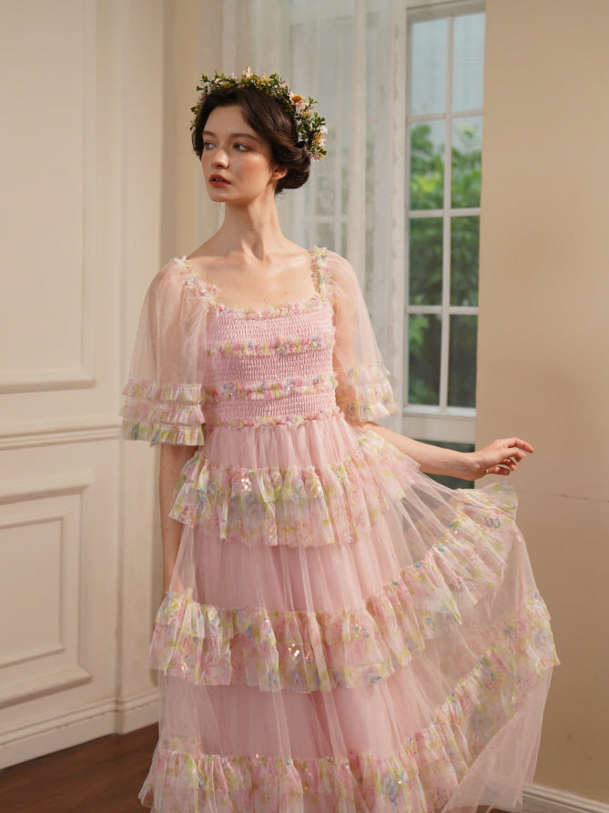 Dressed in a sheer pink ruffle gown, the model gently lifts the skirt with one hand, capturing an elegant princesscore mood near a sunlit window.