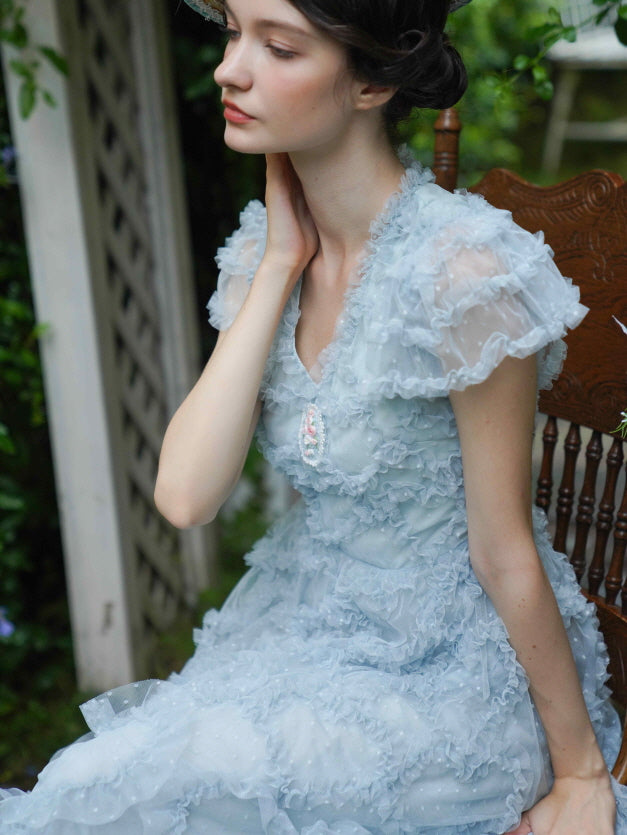 Close-up of a model in a pastel blue ruffle dress with flutter sleeves and vintage cameo brooch, radiating soft coquette and princesscore vibes.