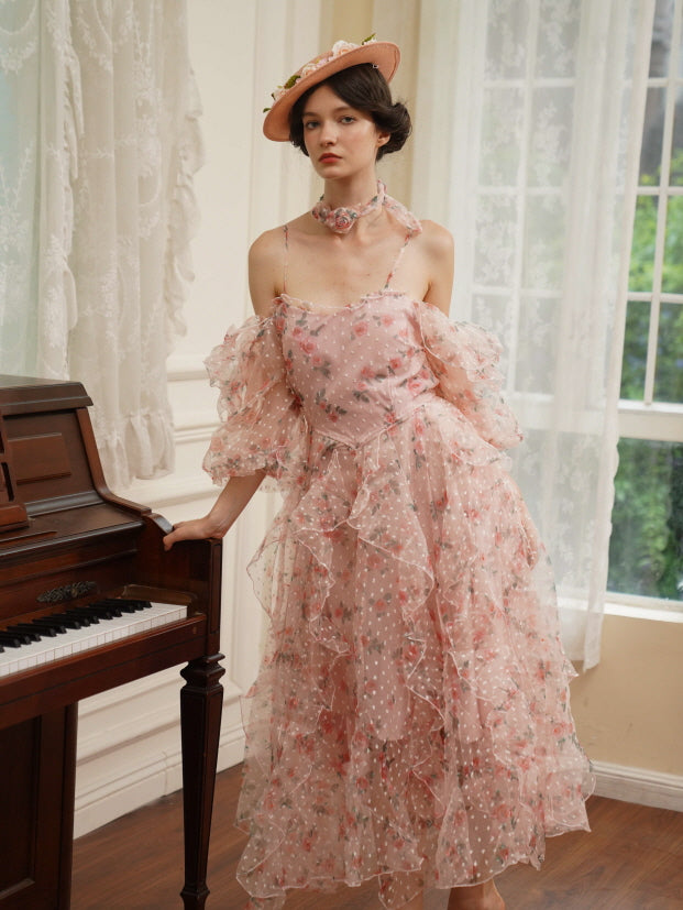 A model in a soft pink layered floral dress leans on a piano, styled in princess vintage fashion with delicate textures and a dreamy silhouette.