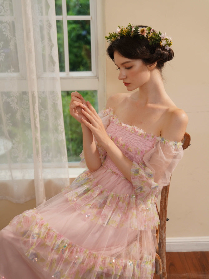 Seated in a pink ruffled fairycore dress, the woman looks at her hands quietly, surrounded by soft light and romantic vintage details.