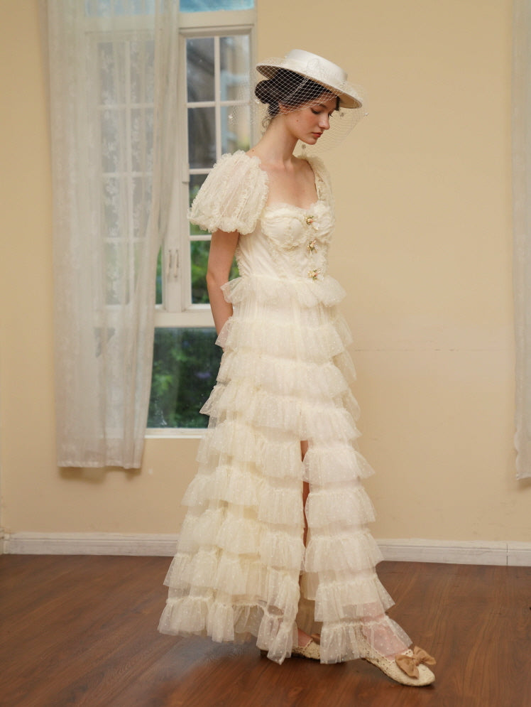 Model in an ivory tiered tulle dress with puff sleeves and floral bows stands by a window, exuding vintage elegance and soft princesscore charm.