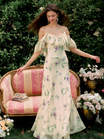 Standing by a vintage sofa in a rose-filled garden, the model wears a soft yellow floral dress with romantic ruffles, perfect for a dreamy summer day.