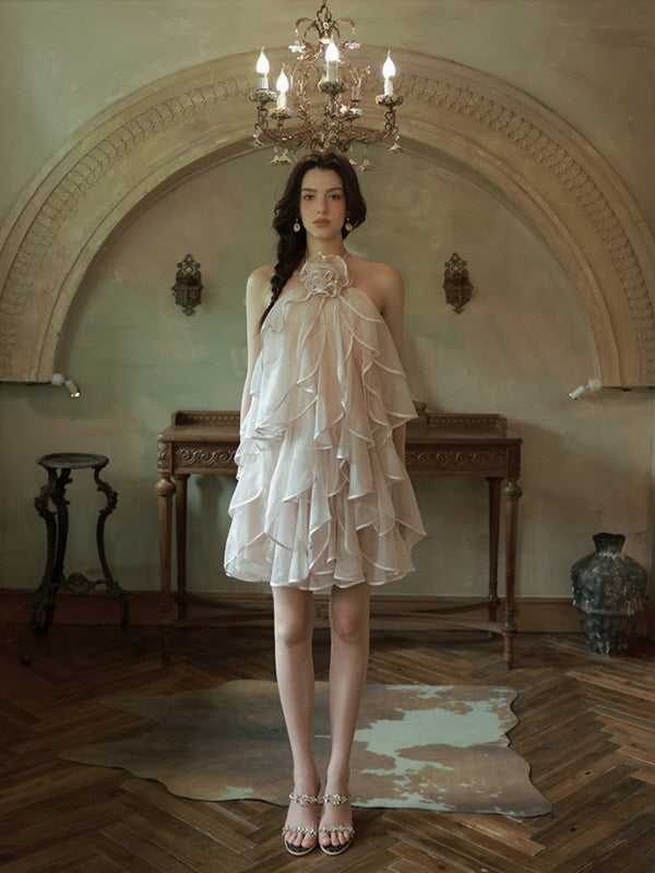 A young woman stands in a vintage-style room wearing a soft pink halter dress with cascading ruffles, evoking a princesscore aesthetic.