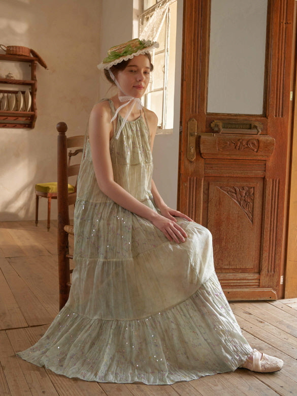 Seated near a wooden door, the woman wears a sparkly tiered dress in soft green, evoking a serene fairycore and romantic countryside mood.