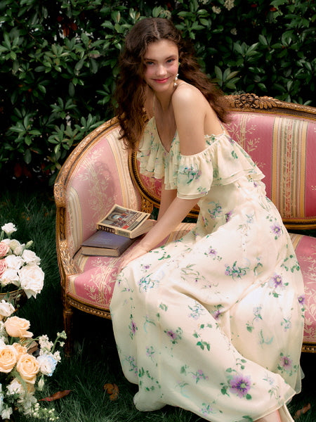 Seated gracefully on a vintage pink sofa, the model wears a soft yellow floral off-shoulder fairycore dress, radiating a romantic summer garden vibe.
