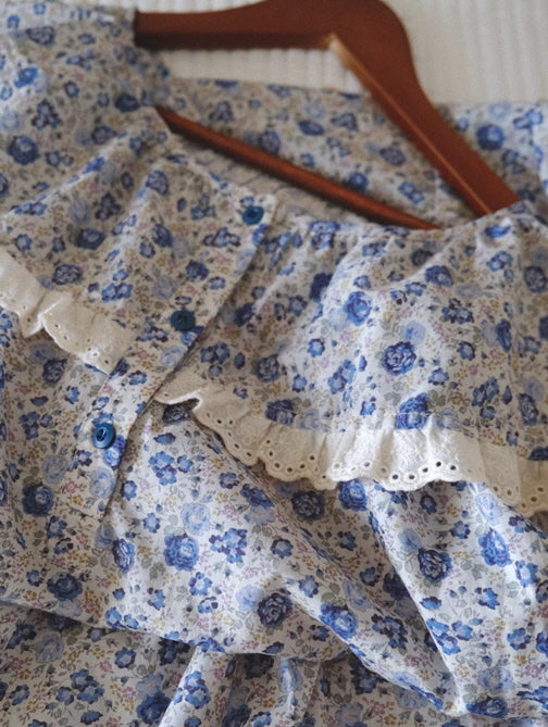 A close-up view of a floral nightgown on a wooden hanger, featuring delicate eyelet lace trim and blue buttons for a vintage-inspired finish.