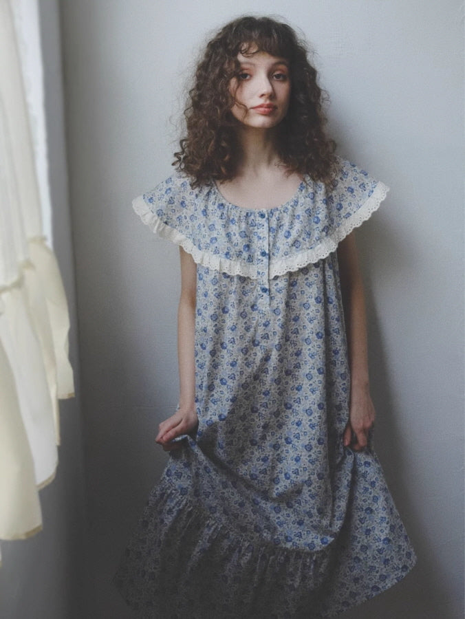 A young woman in a dreamy blue floral nightgown stands near a softly lit window, evoking a fairytale morning in a cottagecore aesthetic.