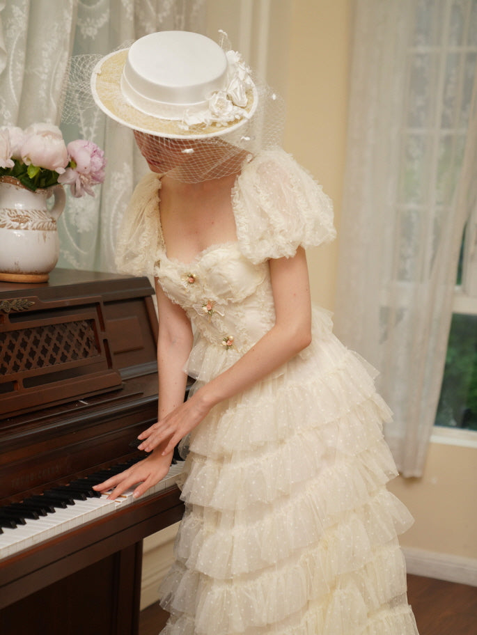 Model in a layered ivory tulle dress plays the piano, adorned with floral bows and puff sleeves, evoking a soft vintage and princesscore elegance.