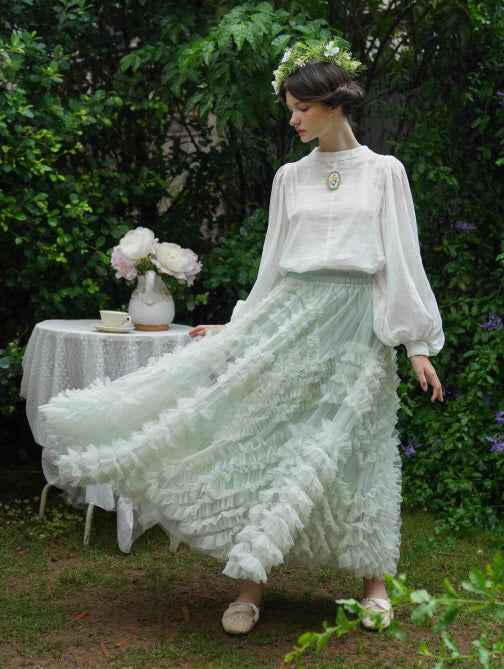 The model twirls in a mint green ruffle skirt and white blouse with a floral brooch, capturing a soft and whimsical fairycore atmosphere.