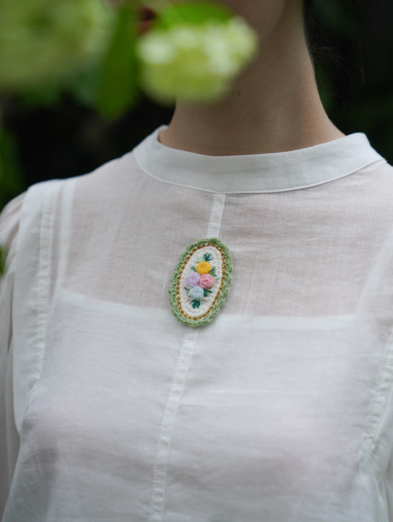 Close-up of a white blouse with a floral embroidered brooch, highlighting delicate textures and fairycore detailing in soft natural light.