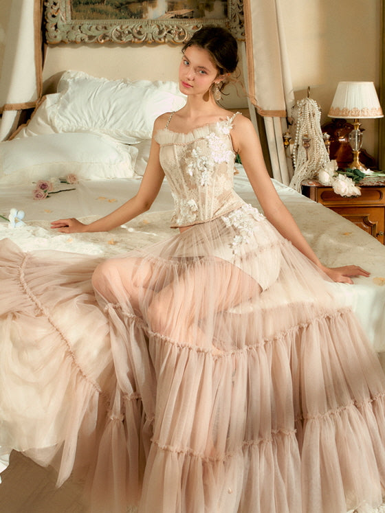 A young woman sits gracefully on a vintage-style bed, wearing a blush pink floral corset with a sheer layered tulle skirt, embodying a fairytale princesscore mood.
