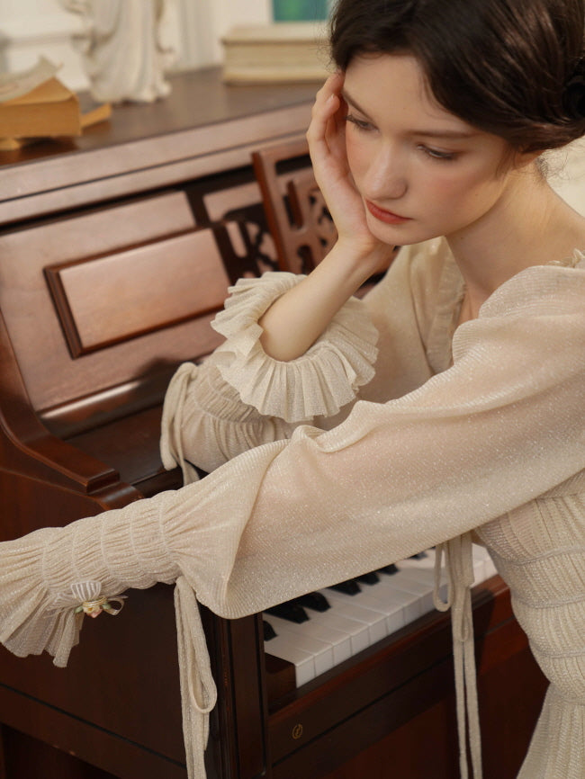 Resting pensively by the piano, a model in a vintage-style cream dress with gathered sleeves evokes a delicate and dreamy atmosphere.