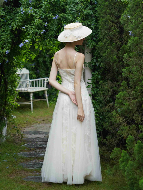 Back view of a woman walking through a garden archway in a flowing white fairycore dress and sunhat, exuding vintage fairytale charm.