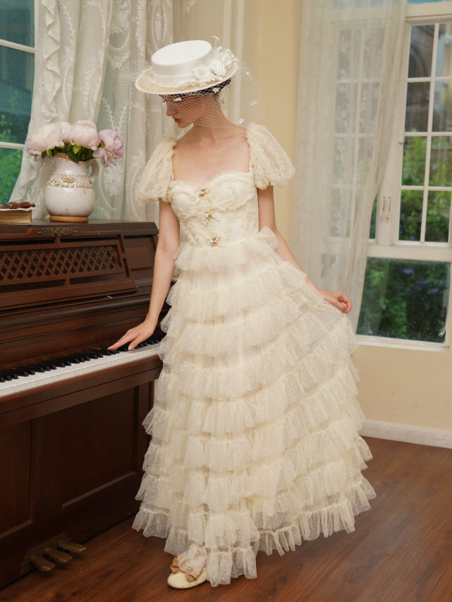 Model poses beside a piano in a ruffled ivory dress with puff sleeves and floral bows, expressing delicate vintage grace and fairytale  beauty.