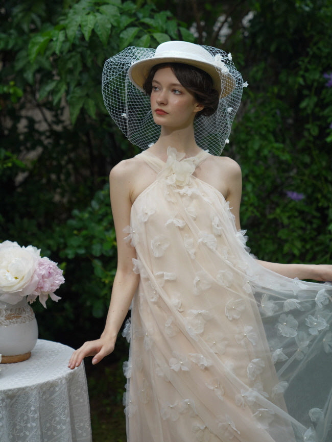 Model in a sheer floral beige dress and netted white hat poses beside a lace table, creating a vintage fairycore daydream in soft light.
