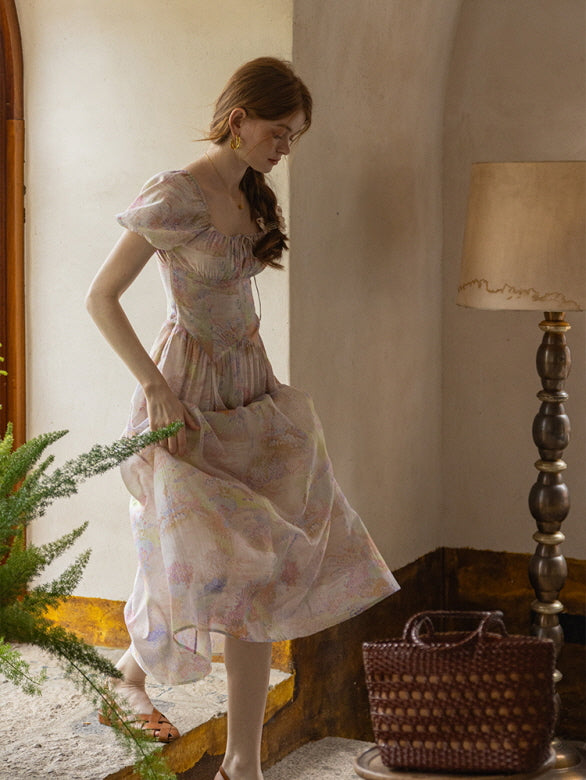 A woman steps gracefully down a rustic staircase in a flowing pastel floral dress, capturing a soft, fairytale-inspired aesthetic.