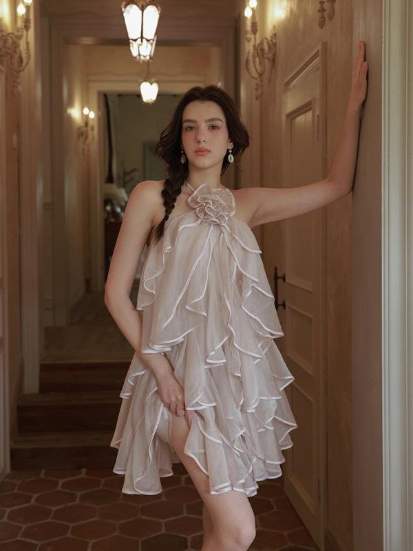 Leaning softly against the hallway wall, the model wears a layered blush dress with a floral halter neckline, evoking a coquette and dreamy look.